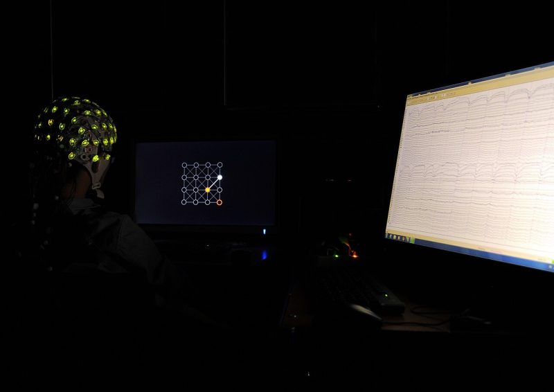 Archivfoto: Brain-computer interface experiment. The participant (left) is wearing an EEG cap. Their brain activity (right) is recorded and interpreted in real time to steer a cursor on the screen (middle).